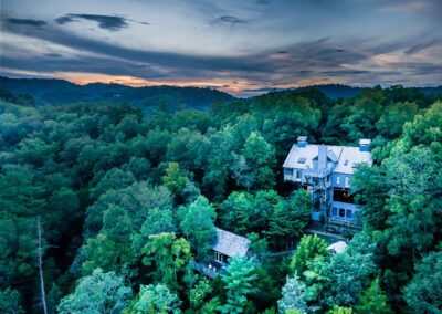Aerial twilight photo of Laurel Valley Mountain Retreat surrounded by dense forest and distant Smoky Mountain ridgelines under a colorful evening sky.